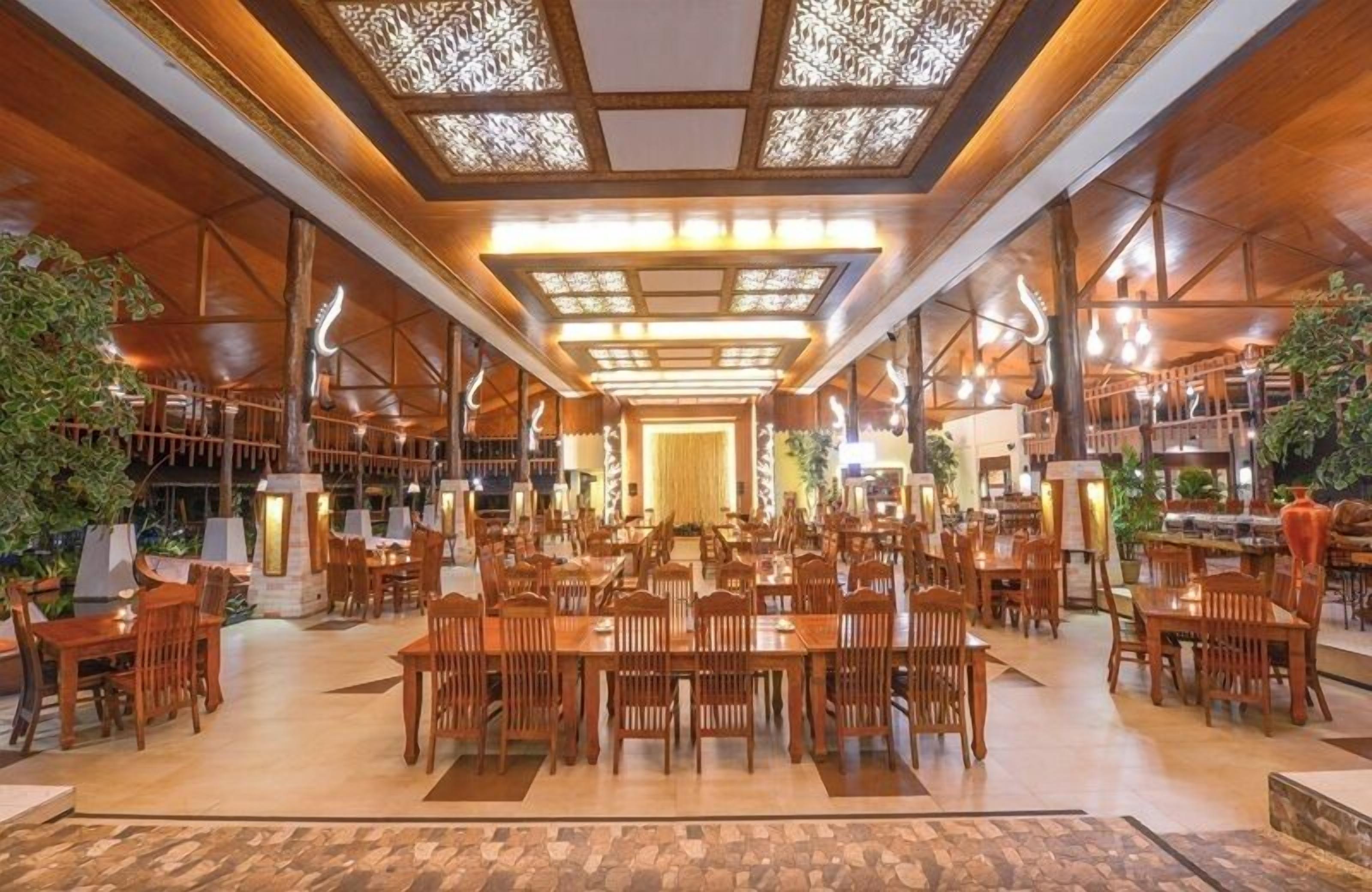 A spacious dining area with wooden tables and chairs, a central walkway, and decorative lighting.