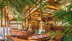 Un restaurant amb vaixells de fusta com a taules, envoltat de palmeres altes i un sostre elevat.