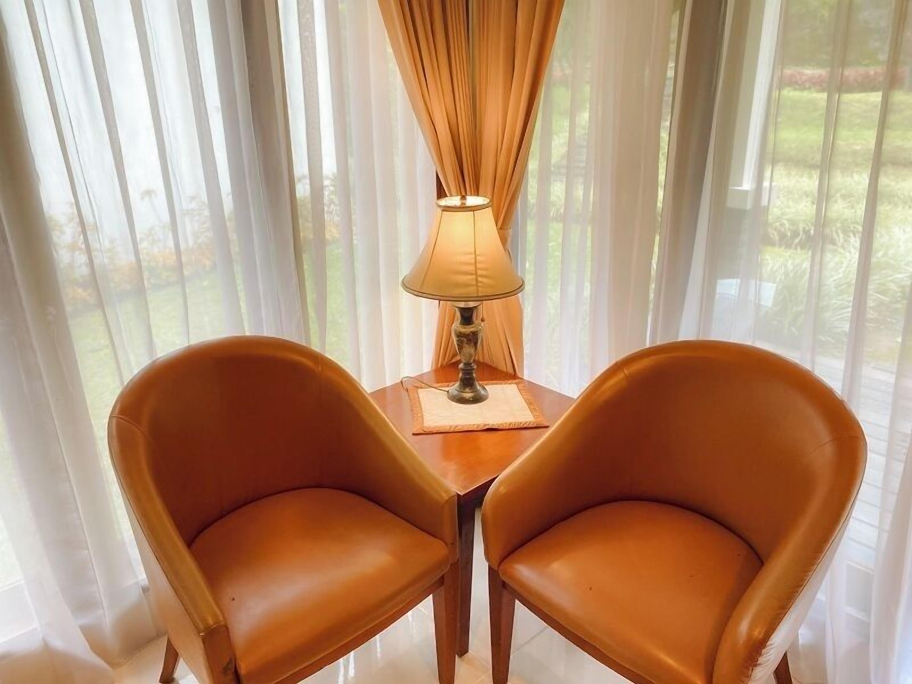 Zwei Stühle, ein Tisch und eine Lampe in einem Raum mit transparenten Vorhängen und Blick auf Grünflächen.
