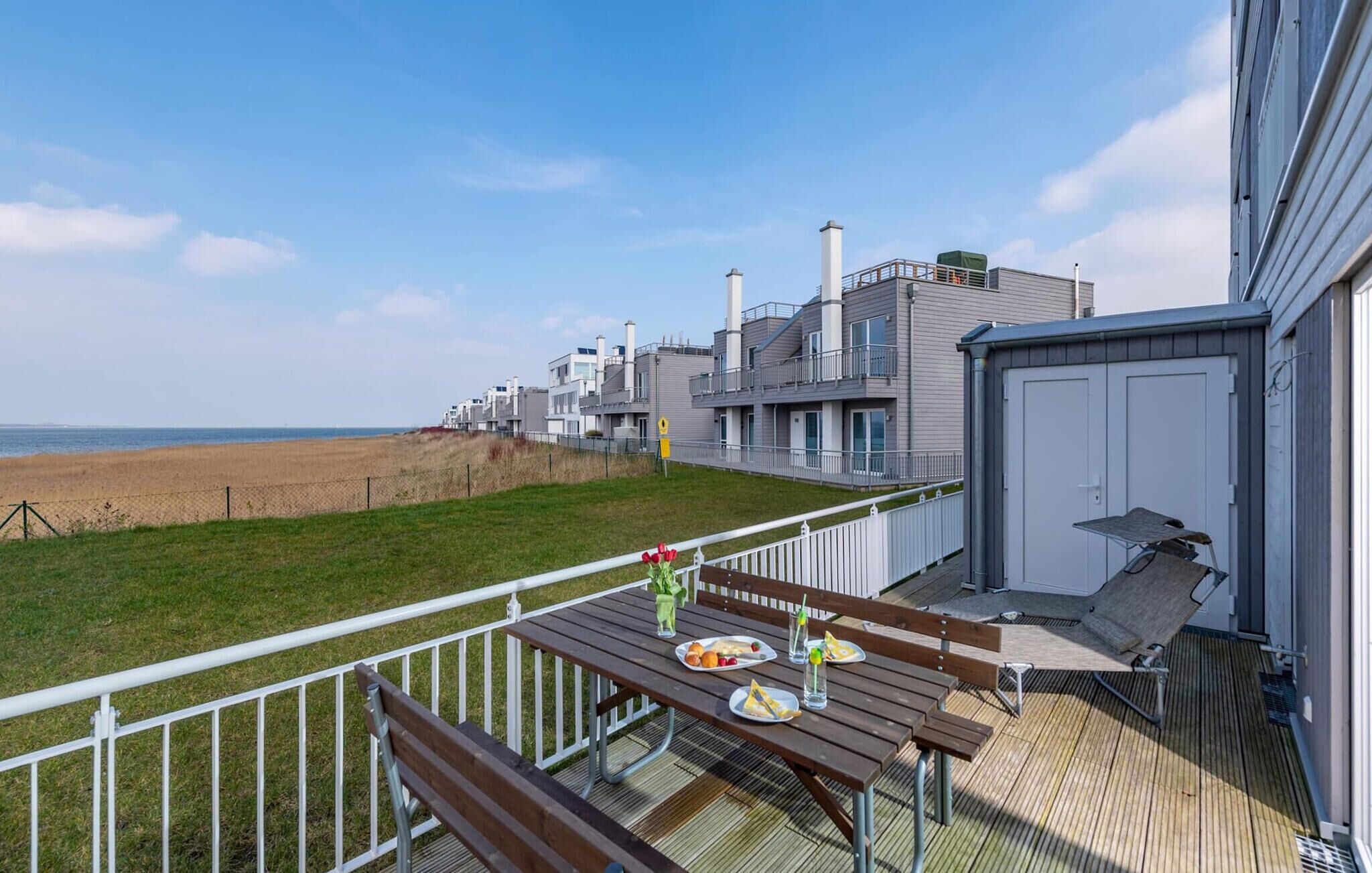 Une terrasse avec une table dressée pour deux personnes, offrant une vue sur une plage et des bâtiments modernes.