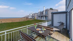Een terras met een tafel voor twee, met uitzicht op een strand en moderne gebouwen.
