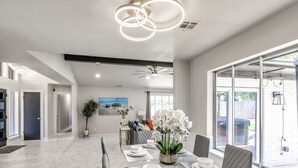 A spacious dining area with a long table set for six, a ceiling fan, and large windows offering a view of the outdoors.