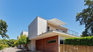 A modern two-story house with a flat roof, large windows, and a balcony.