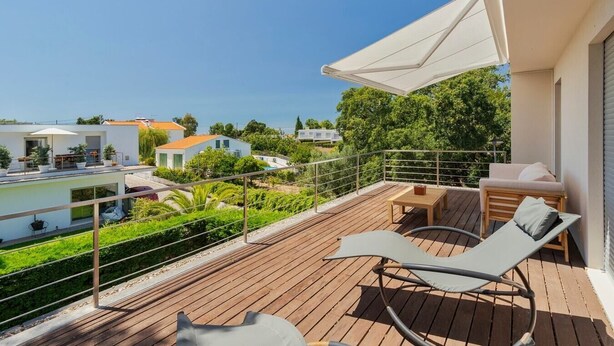 A balcony with a wooden deck, two lounge chairs, a small table, and a white umbrella.