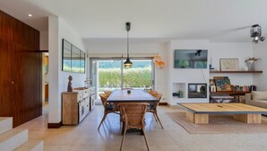 A modern kitchen with a dining area, large windows, and a TV.
