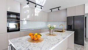 A modern kitchen with a marble countertop, stainless steel appliances, and a central island with a fruit bowl and flowers. - Vacation home Noel by Interhome (Imotski)