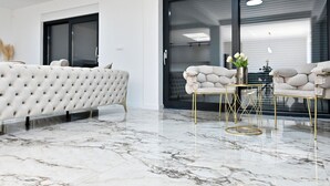A modern living room with a white tufted sofa, a gold-framed coffee table, and a large sliding glass door. - Vacation home Noel by Interhome (Imotski)