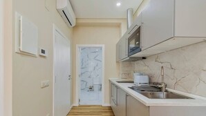 A narrow kitchen with a marble backsplash, a built-in microwave, and a stainless steel sink.