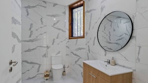 A bathroom with marble walls, a wooden vanity, a round mirror, and a window.