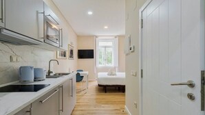 A compact hotel room with a kitchenette, a bed, and a large window.