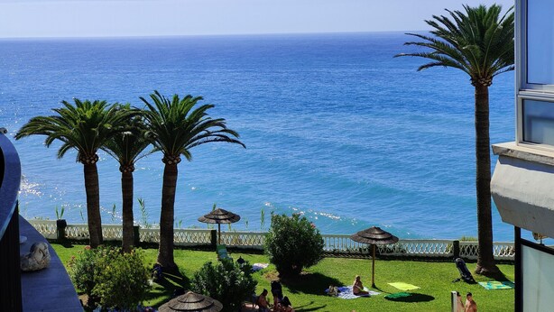A balcony with a view of the ocean, palm trees, and a pool area with umbrellas. - AP408 ACAPULCO PLAYA SM NERJA (Nerja)
