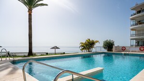 A swimming pool with a view of the ocean, a palm tree, and a building with balconies. - AP408 ACAPULCO PLAYA SM NERJA (Nerja)