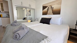 A hotel room with a bed, a mirror, a painting, a desk with a lamp, and a kitchenette. - AP408 ACAPULCO PLAYA SM NERJA (Nerja)