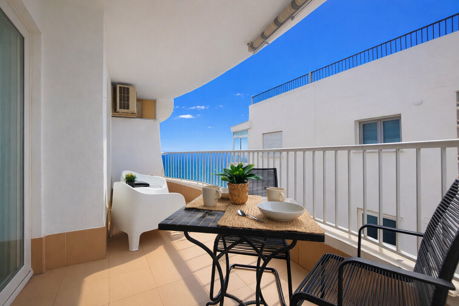 A balcony with a table, chairs, and a potted plant.