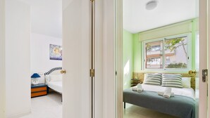 A hotel room with a bed, a bedside table with a lamp, and a window with a view of buildings. - WELCS APARTAMENTO 170 PDA en el puerto (Platja d´Aro)