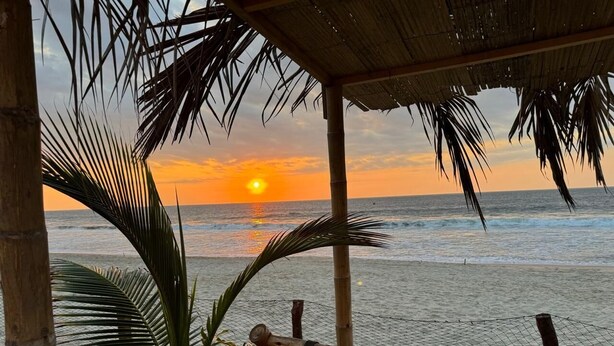 A beach view with a wooden chair and a thatched roof structure. - Hab21 Hotel in front of the sea, ideal to enjoy the sun and relax with Wifi and AC (Canoas de Punta Sal)