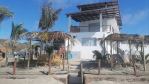 A beachside building with a white exterior, a wooden staircase leading to a balcony, and palm trees around. - Hab21 Hotel in front of the sea, ideal to enjoy the sun and relax with Wifi and AC (Canoas de Punta Sal)
