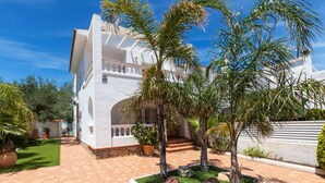 A white villa with a tiled patio, palm trees, and a well-maintained lawn.