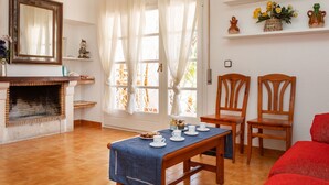 A living room with a fireplace, a dining table set with cups and saucers, two wooden chairs, and a red sofa.