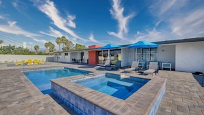 A swimming pool with a tiled edge, outdoor seating, and umbrellas.