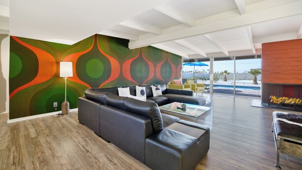 A modern living room with a black leather sofa, a coffee table, and a colorful abstract wall.