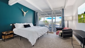 A bedroom with a bed, a desk, a chair, a large window, and a wall-mounted skull.