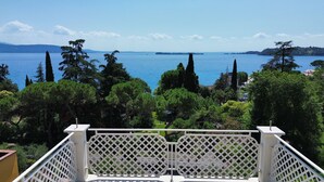A balcony with a lattice railing overlooking a body of water, surrounded by trees and buildings. - Villa Diamante By Bookinggardalake (Salò)