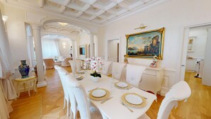 A formal dining room with a long table set for a meal, white chairs, and a painting on the wall. - Villa Diamante By Bookinggardalake (Salò)