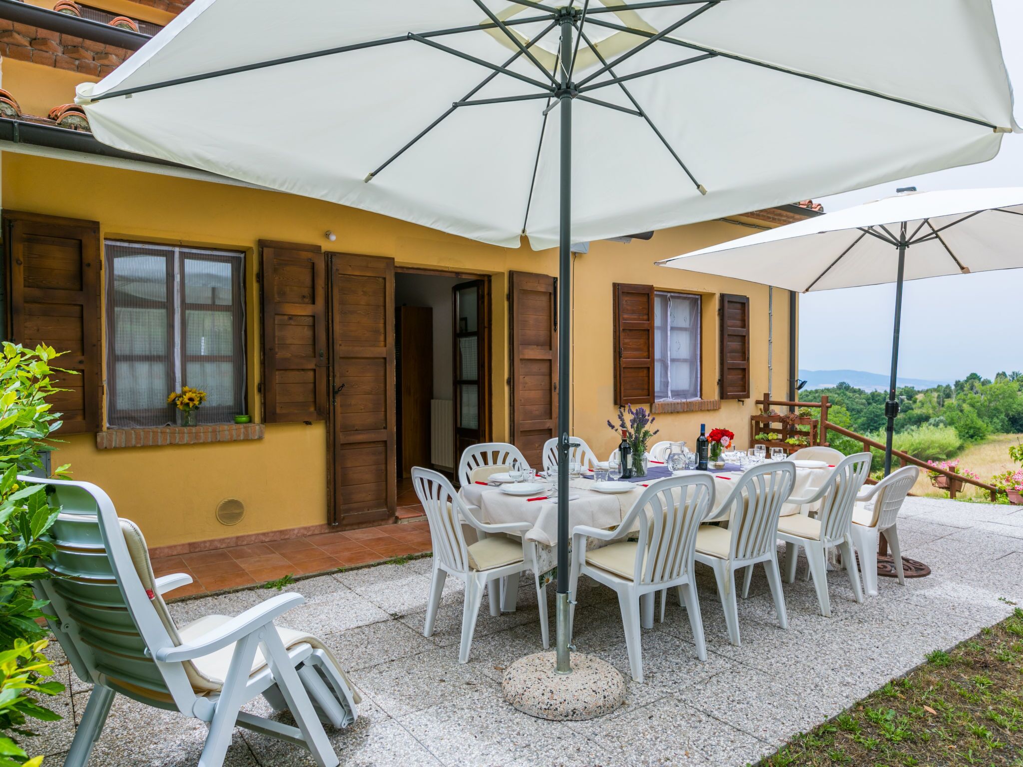 A patio with a table set for dining, surrounded by white chairs and a large umbrella.