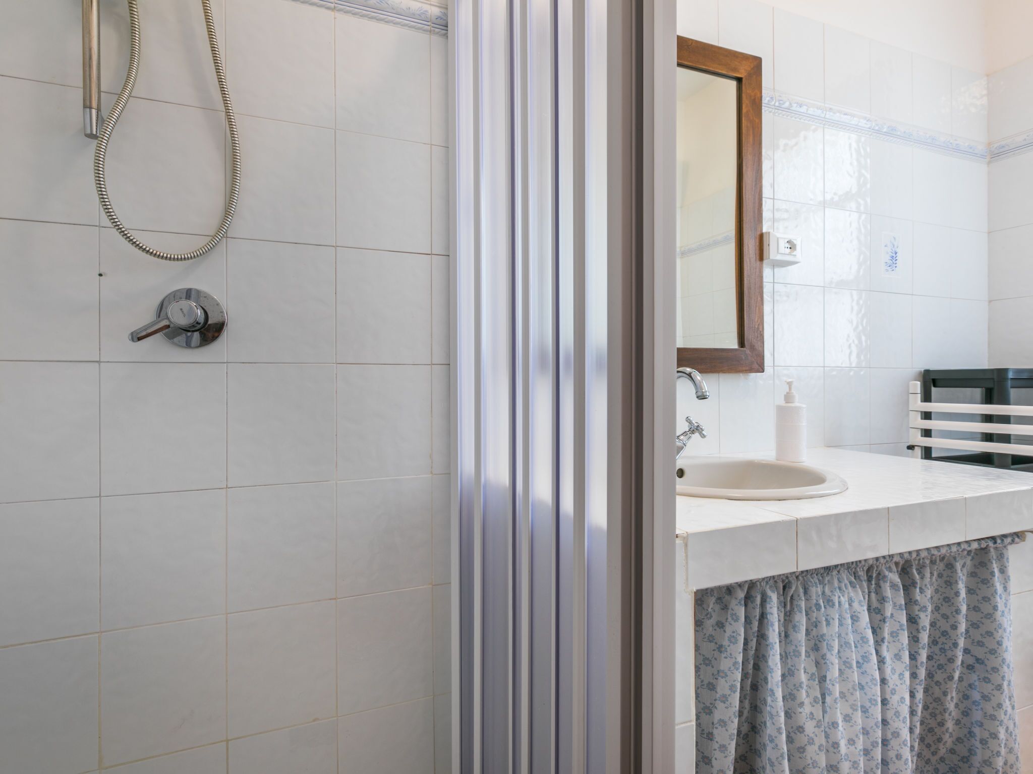 Een badkamer met douche, wastafel en spiegel.