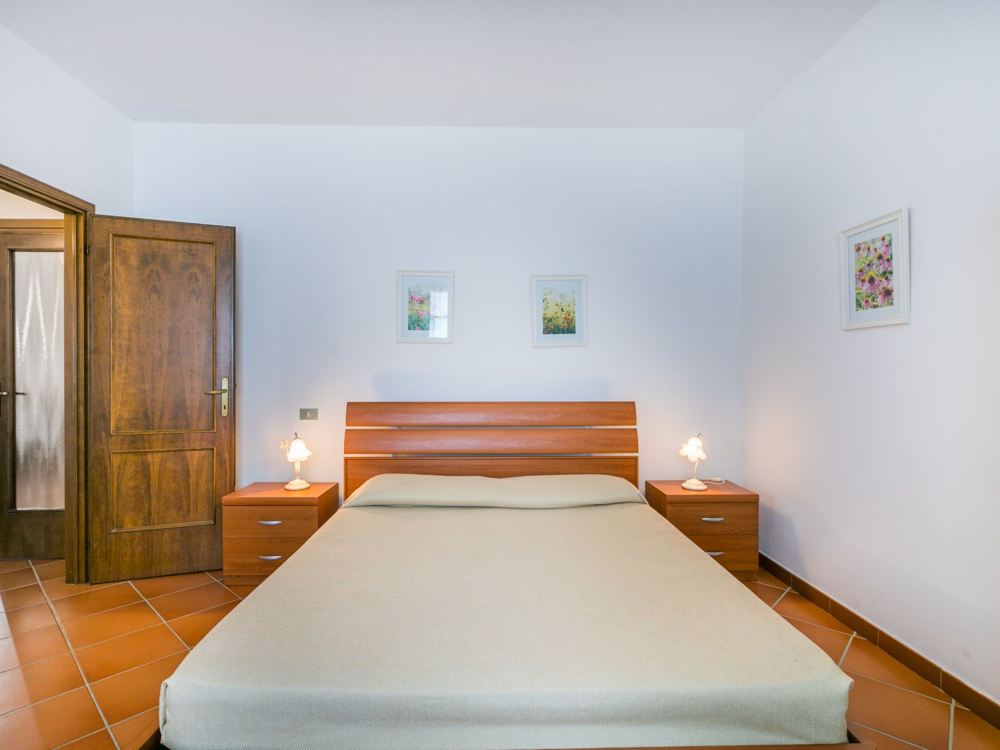 Ein Schlafzimmer mit einem hölzernen Bett, zwei Nachttischen mit Lampen, einem Holzschrank und zwei gerahmten Bildern an der Wand.