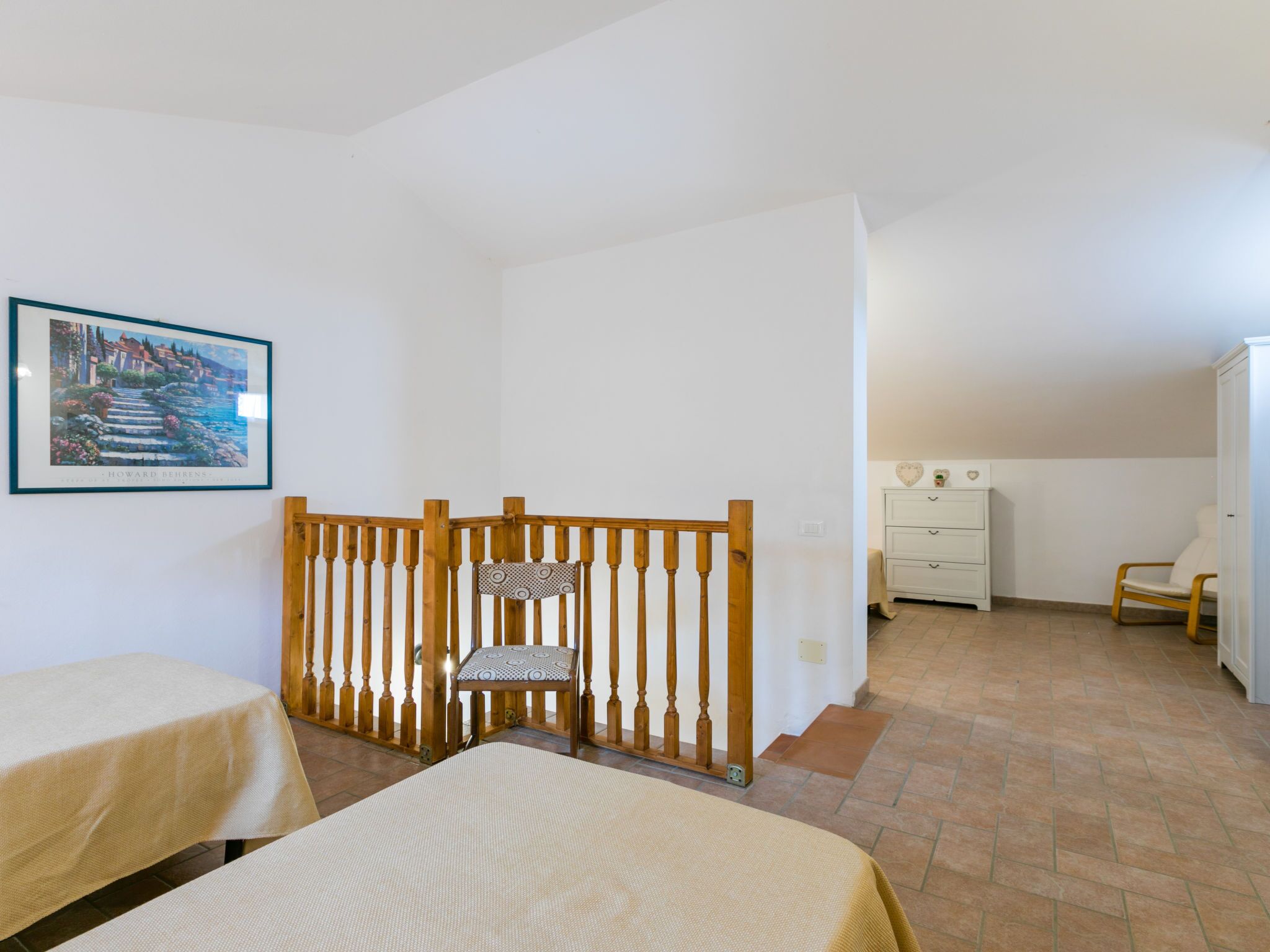 A room with two beds, a wooden chair, a dresser, and a framed picture on the wall.
