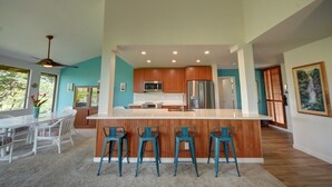 Una cocina moderna con armarios de madera, una isla central con taburetes y una zona de comedor con una mesa y sillas blancas.