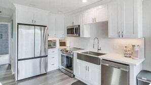 A modern kitchen with white cabinetry, stainless steel appliances, and a compact layout. - Waterfront Cozy Unit Bay St Louis / kayaks &dock (Bay St. Louis)