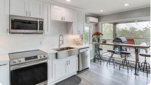 A modern kitchen with white cabinets, a stainless steel microwave, a built-in oven, a sink, and a bar area with stools. - Waterfront Cozy Unit Bay St Louis / kayaks &dock (Bay St. Louis)