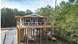 A wooden deck structure with a covered area, surrounded by trees and a clear sky. - Waterfront Cozy Unit Bay St Louis / kayaks &dock (Bay St. Louis)
