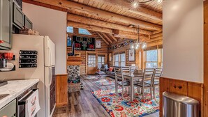 A rustic cabin interior with a kitchen, dining area, and a large window.