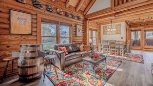A log cabin interior with a leather sofa, dining table, and a large wooden barrel.