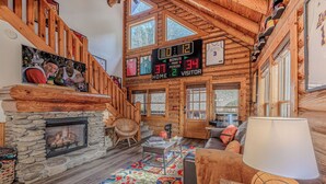 A cozy log cabin interior with a stone fireplace, a wooden staircase, and a basketball-themed wall art.