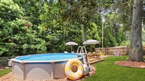 Una piscina sense soterrar amb una escala, envoltada per un pont de fusta i protegida per ombrelles.
