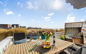 A wooden deck with a table set for dining, featuring a fruit bowl, glasses, and a vase of flowers. - Nice home in Olpenitz with sauna (Olpenitz)