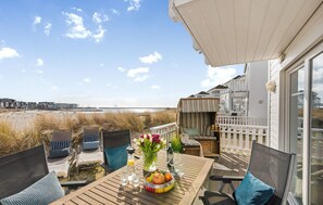 A wooden deck with a table set for dining, overlooking a beach and residential buildings. - Nice home in Olpenitz with sauna (Olpenitz)
