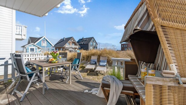 Une terrasse en bois avec une table et des chaises, un fauteuil en osier et une vue sur les maisons au loin.