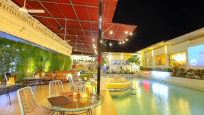Un espace extérieur avec une piscine, des tables et des chaises, un coin salon abrité et un bar.