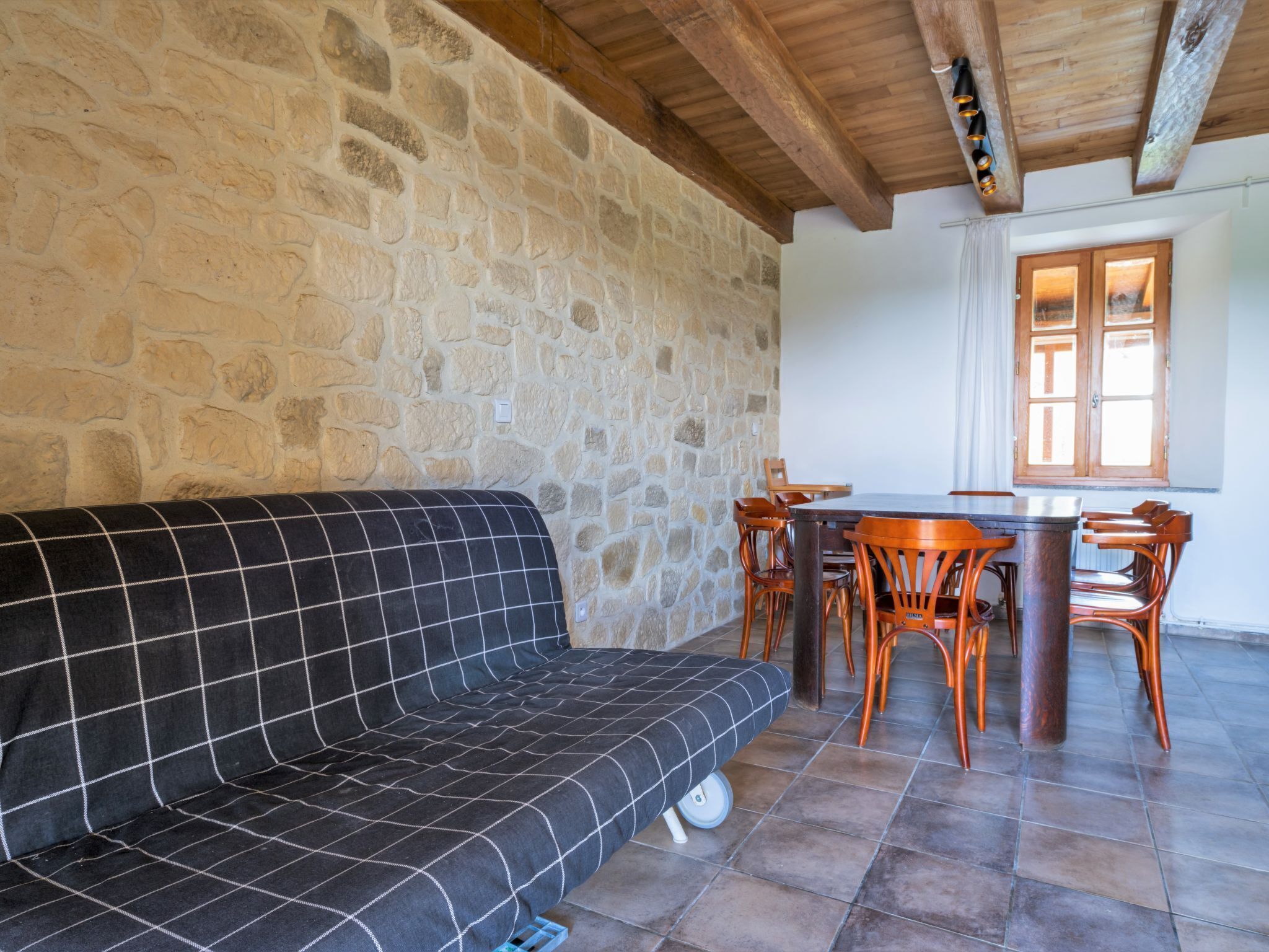A stone-walled room with a black sofa, wooden dining table, and chairs.