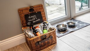 A wicker basket with a sign reading "doggy towels & blankets" containing dog supplies and a pet bowl mat with two bowls.