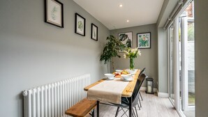 A dining area with a long table, benches, and framed botanical prints on the wall.
