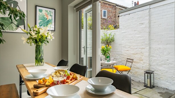 A dining area with a table set for four, a vase of flowers, and a view of the backyard.