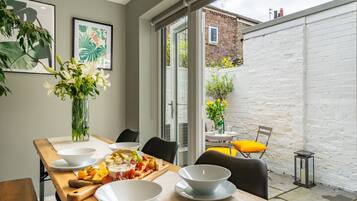 A dining area with a table set for four, a vase of flowers, and a view of the backyard.