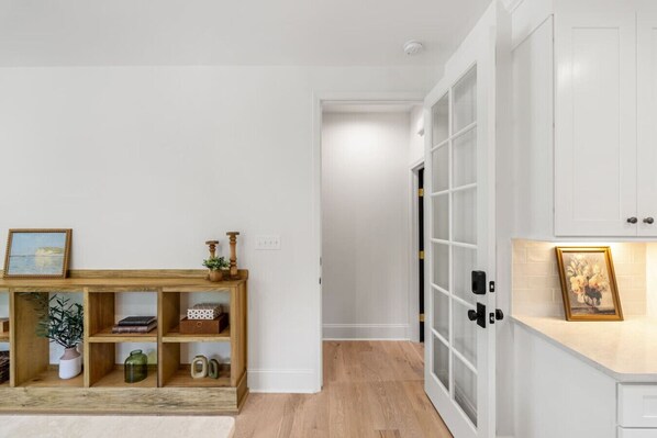 A hallway with a wooden console table, a white door with glass panels, and a white cabinet with a picture frame.
